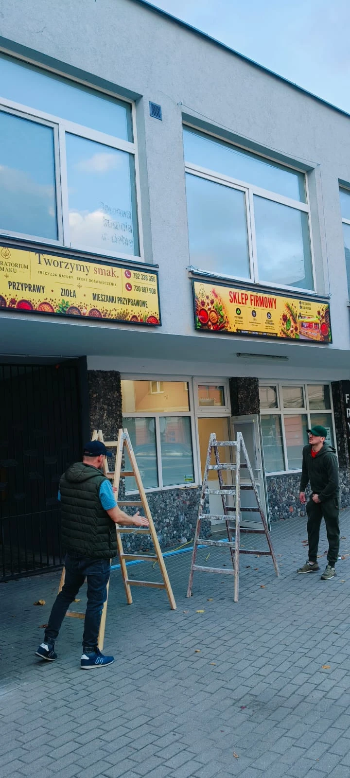 Dwa szyldy Laboratorium Smaku zamontowane na elewacji, obok drabiny